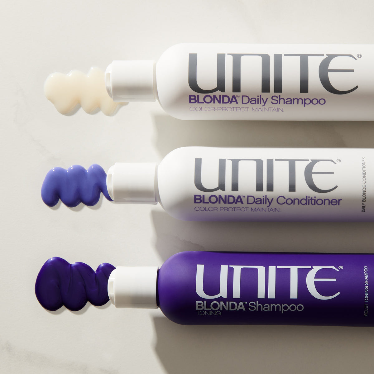 Bottles of Unite BLONDA Daily Shampoo, purple conditioner, and toning shampoo with swatches of each product on a white surface.