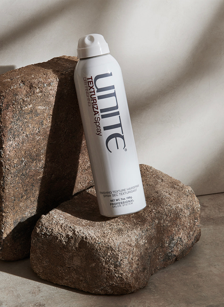 Bottle of texturizing spray hair product displayed on stone blocks in natural light.