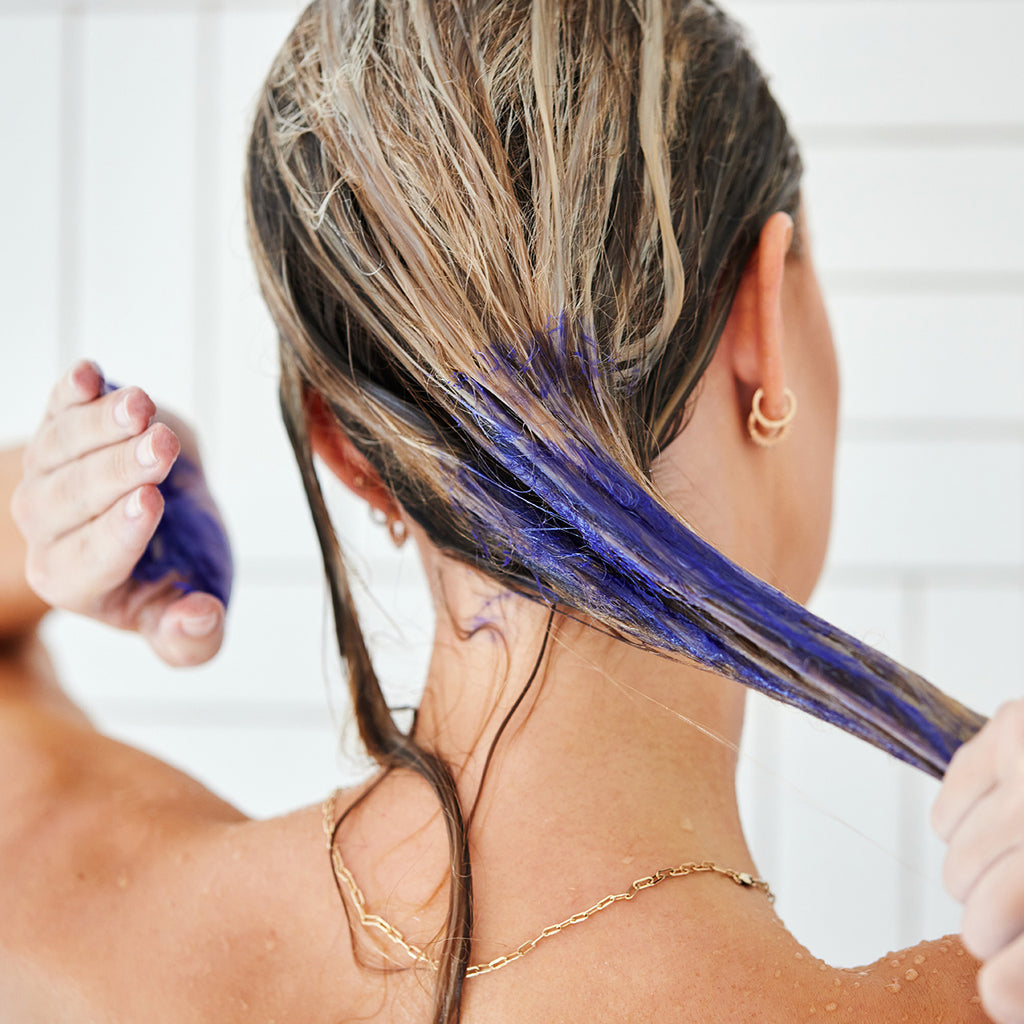A woman using purple shampoo to wash her hair in the shower